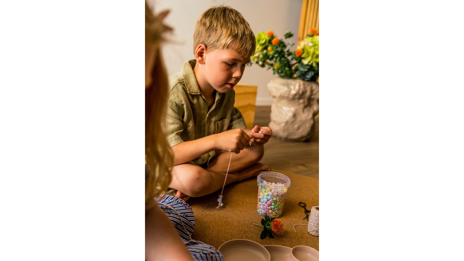 Barn sidder på gulv og leger med perler og perleplader i varme pastelagtige farver.